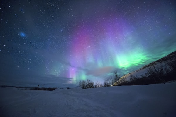 Purple and green aurora borealis over a snowy valley under a starry night sky.