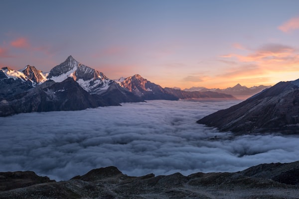 Snow-capped mountain peaks rising above a thick sea of clouds at sunrise.