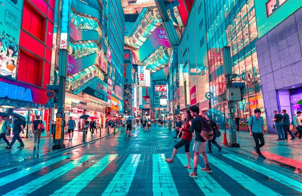 Crowded neon-lit Akihabara Tokyo street at night with glowing digital billboards.